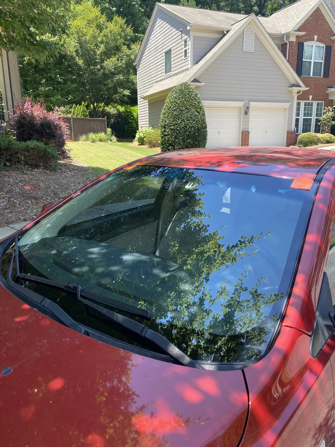 Red sedan windshield replacement in a driveway